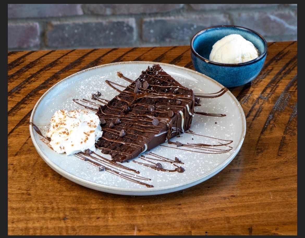 Slice of chocolate cake with whipped cream and a bowl of vanilla ice cream