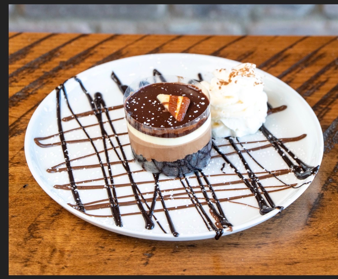 Layered triple chocolate mousse cup with whipped cream and chocolate drizzle