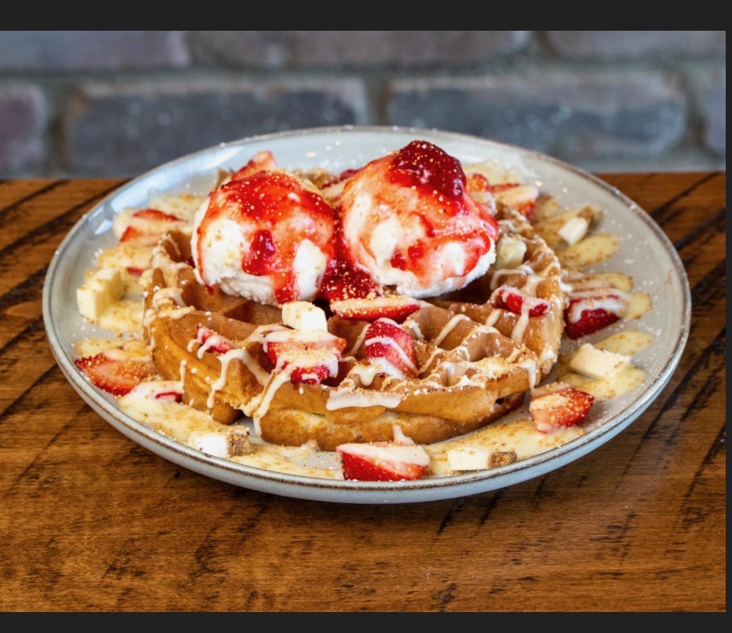 Belgian waffle topped with ice cream scoops, fresh strawberries and white chocolate drizzle